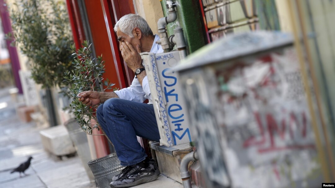 Một người đàn ông ngồi trên bậc thềm trước cửa hàng của mình ở trung tâm Athens, Hy Lạp sau vụ khoảng.